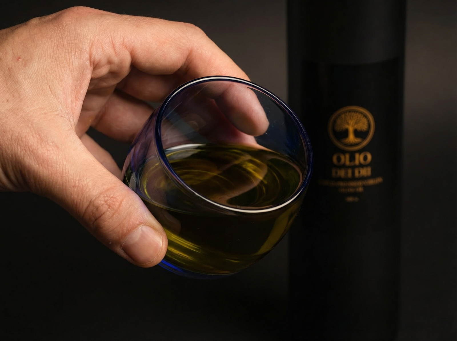 Hand hält ein Glas mit hochwertigem Olivenöl bei der Verkostung – leicht bitteres, grünes Olivenöl mit intensiver Farbe